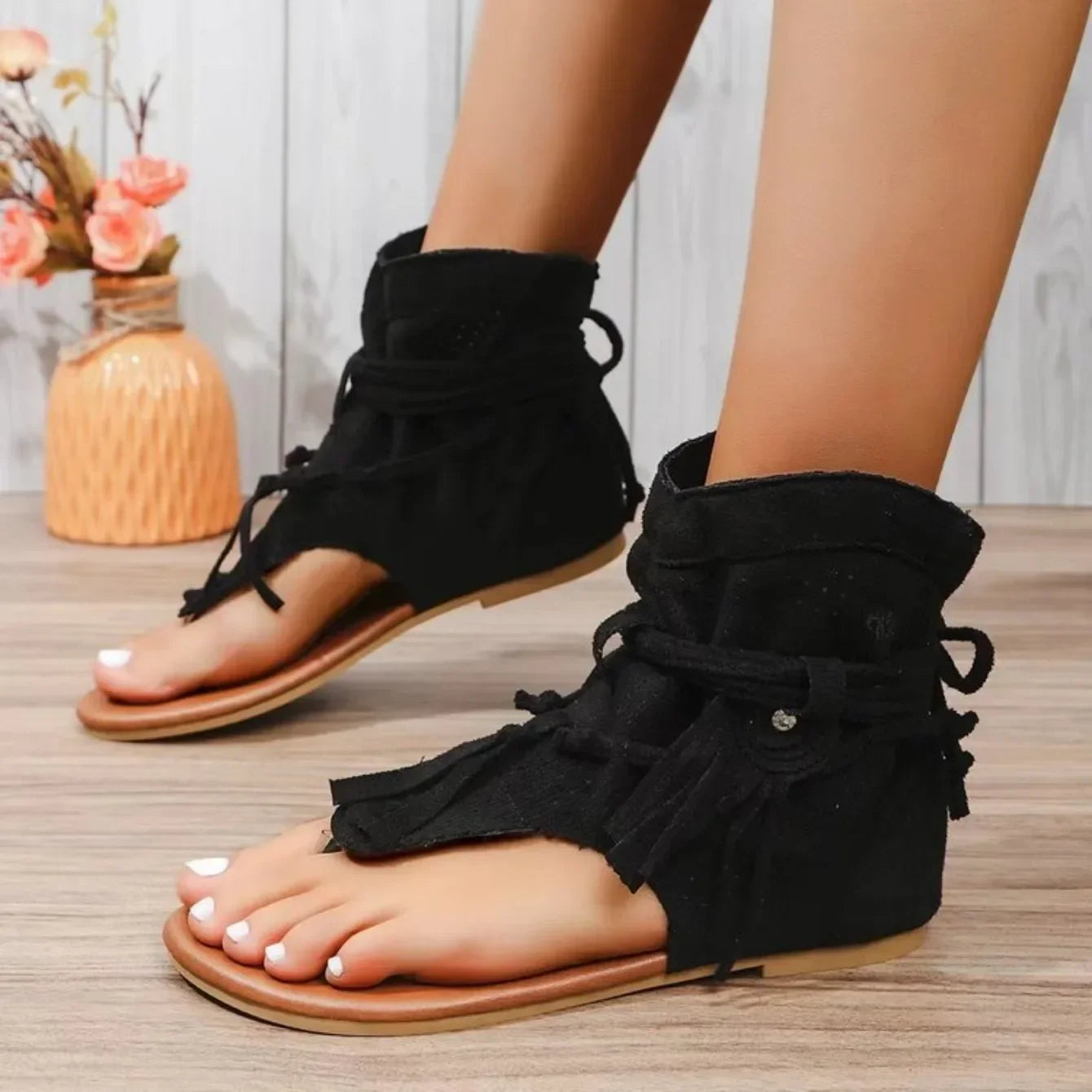 Black sandals with ruched sides worn by a person on a wooden floor.