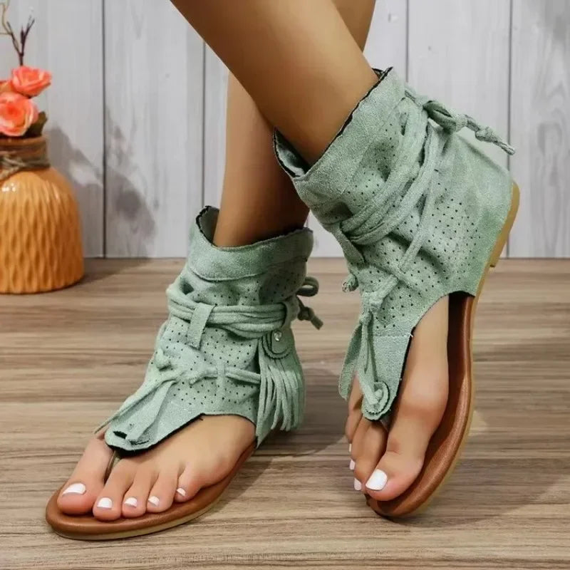 Green sandals with brown soles worn by a person on a wooden floor.